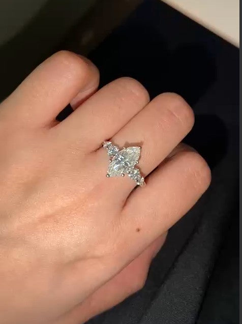 ماركيز-shaped diamond ring on a hand against a dark background
