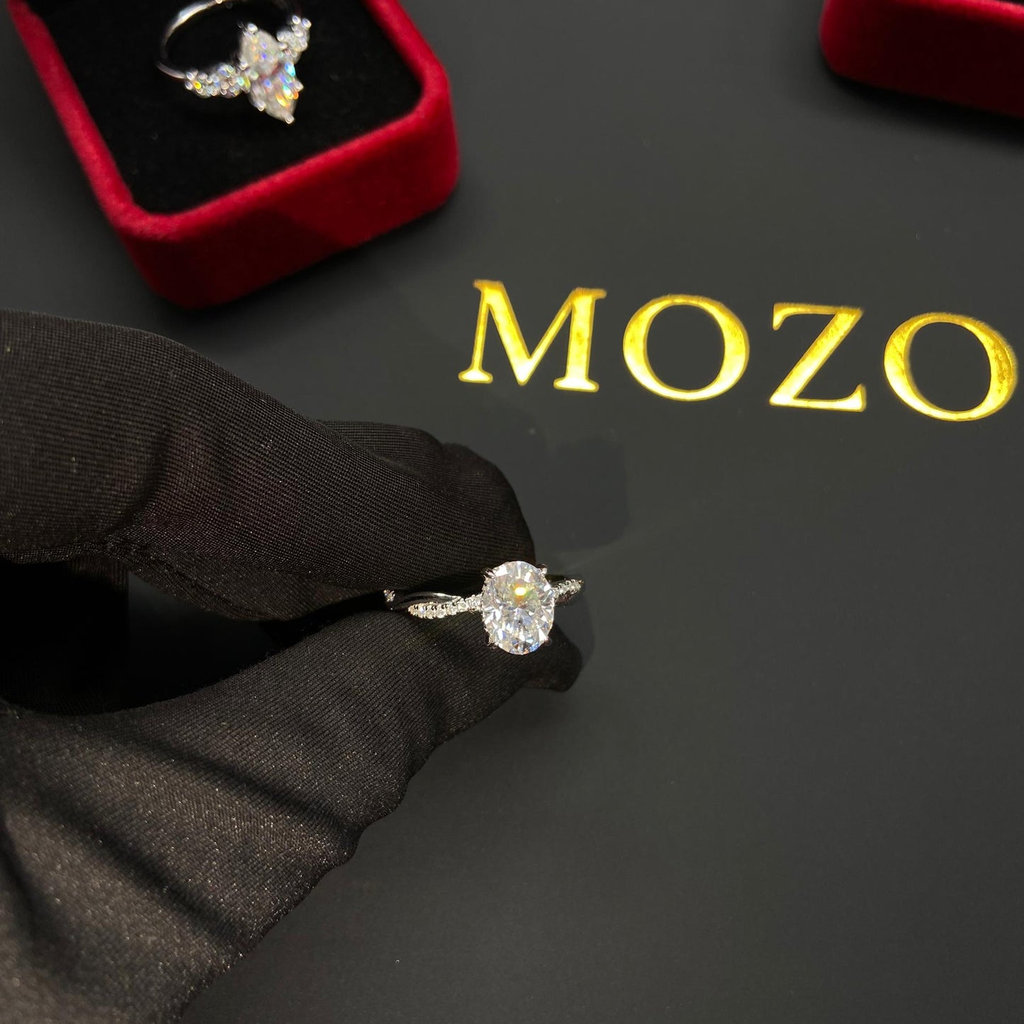 Diamond ring on a black surface with 'MOZO' branding, surrounded by jewelry boxes.