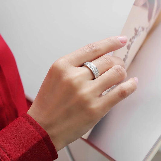 Hand wearing a silver ring with a red sleeve against a neutral background