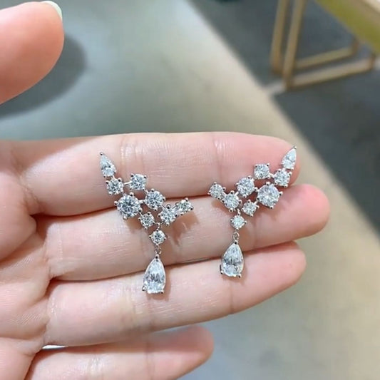 Diamond earrings held between fingers against a blurred background