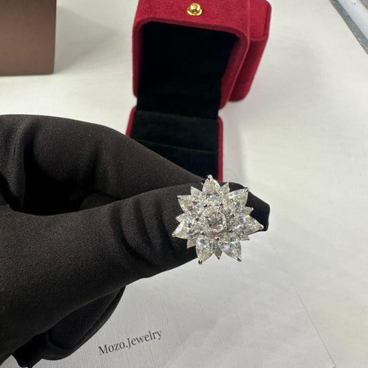 Diamond flower ring held by a gloved hand with a red jewelry box in the background